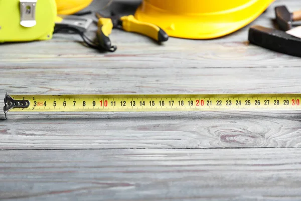Ahşap arka planda inşaat malzemeleriyle şerit ölçümü