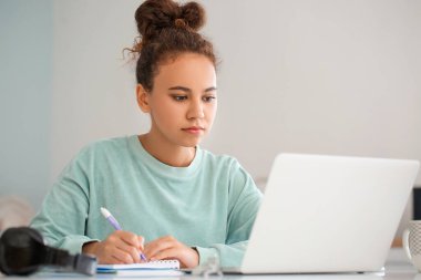 Evde online öğrenim için dizüstü bilgisayar kullanan genç bir kadın