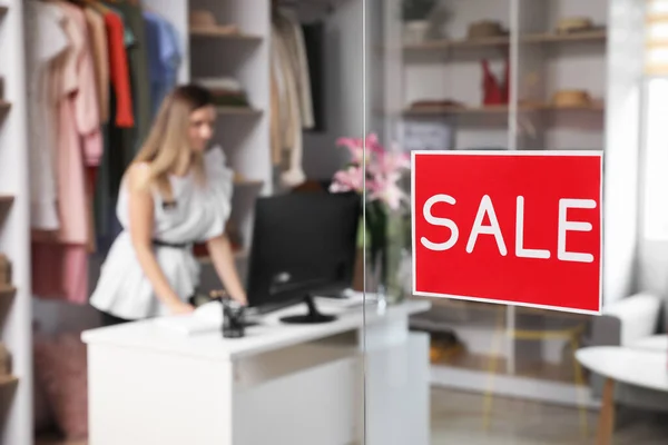 Sticker with word SALE on transparent door of modern clothes store