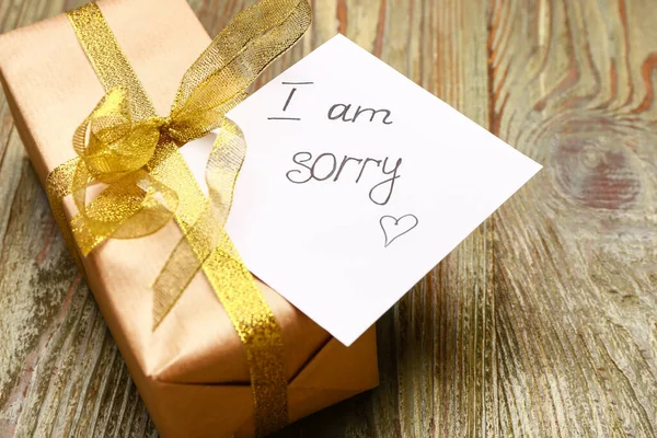 Gift with text I AM SORRY on wooden background