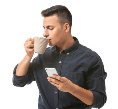 Beyaz arka planda bir fincan çay ve cep telefonu olan yakışıklı bir genç.