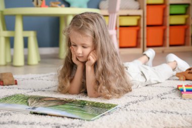 Evde kitap okuyan sevimli küçük bir kız.