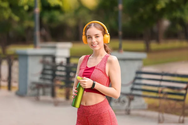 Sporty young woman with headphones and water outdoors
