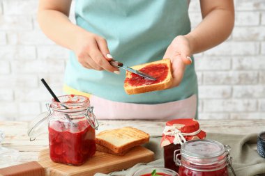 Kadın mutfakta çilek reçeli ile tost yapıyor.