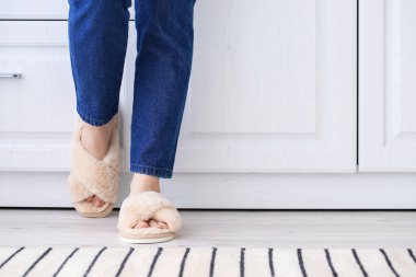 Evde yumuşak terlikli genç bir kadın var.