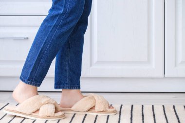 Evde yumuşak terlikli genç bir kadın var.