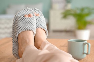 Evde yumuşak terlikli genç bir kadın var.