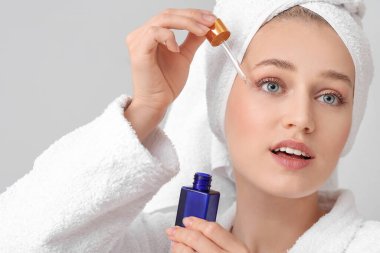 Gri arka planda yüz serumu olan güzel genç bir kadın.