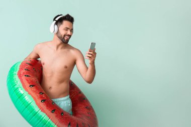 Kulaklıklı, şişirilebilir yüzüklü ve renkli cep telefonlu genç bir adam.