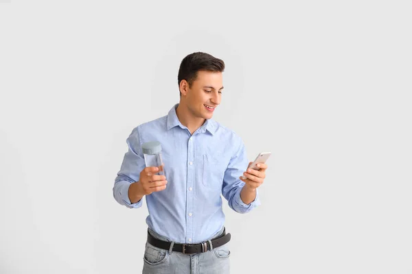 Junger Mann Mit Wasserflasche Und Handy Auf Hellem Hintergrund — Stockfoto