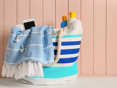 Masanın üzerinde güneş kremi ve cep telefonu olan plaj çantası.