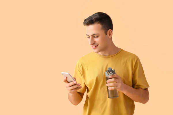 Młody Człowiek Butelką Wody Telefon Komórkowy Tle Koloru — Zdjęcie stockowe