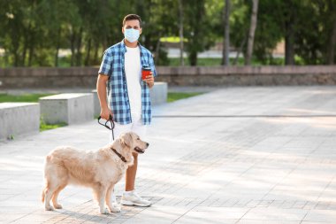 Koruyucu maskeli genç bir adam ve dışarıda sevimli bir köpekle yürüyor.