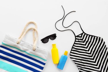 Beyaz arka planda güneş kremi ve aksesuarlı plaj çantası.