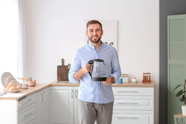 Young man with electric kettle at home