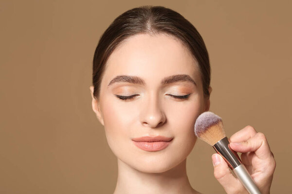 Young woman with makeup brush on color background