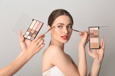 Makyaj sanatçısı, arka planda genç ve güzel bir kadınla çalışıyor.