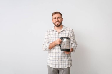 Arka planda elektrikli su ısıtıcısı olan genç bir adam.