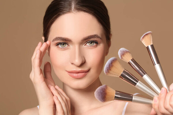 Young woman with makeup brushes on color background