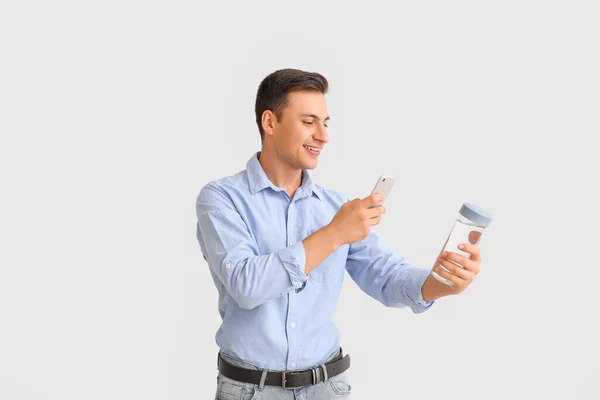 Junger Mann Mit Wasserflasche Und Handy Auf Hellem Hintergrund — Stockfoto