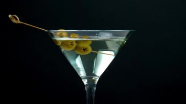 Koyu arkaplanda zeytinli dönen bir bardak martini.