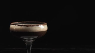 Siyah arka planda dönen bir bardak espresso martini kokteyli, yakın plan.