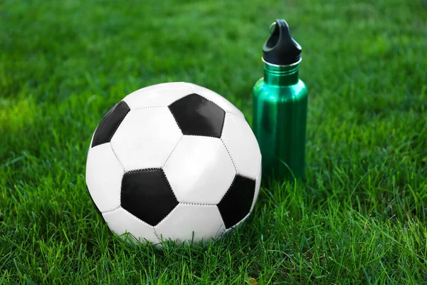 Soccer ball and bottle of water on green grass outdoors