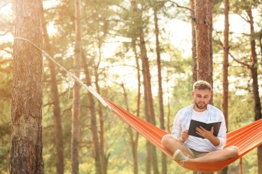Dışarıda hamakta kitap okuyan genç bir adam.