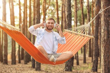 Genç adam dışarıda hamakta dinlenirken müzik dinliyor.