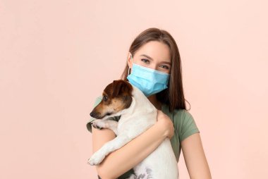 Koruyucu maskeli genç bir kadın ve renkli bir köpeği var.