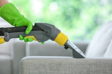 Kuru temizlemecinin çalışanı evdeki kanepedeki kiri temizliyor.