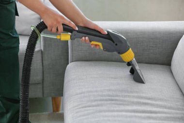 Kuru temizlemecinin çalışanı evdeki kanepedeki kiri temizliyor.