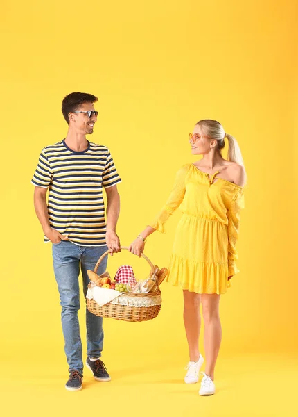 Young couple with food for picnic in basket on color background