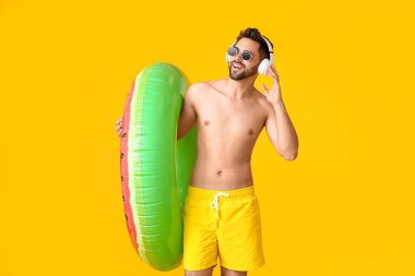 Kulaklık takan ve arka planda şişme yüzük takan genç bir adam.