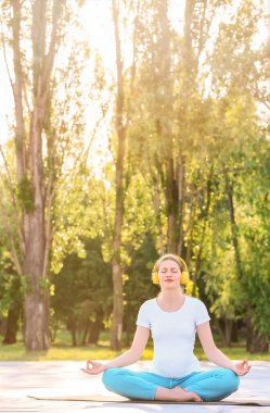 Genç hamile kadın dışarıda yoga yapıyor.