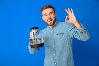 Elektrikli su ısıtıcısı olan genç adam renk arka planında iyi bir hareket gösteriyor.