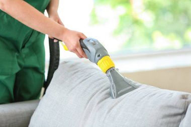 Kuru temizlemecinin çalışanı evdeki kanepedeki kiri temizliyor.