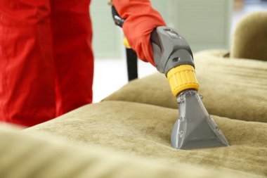 Kuru temizlemecinin çalışanı evdeki kanepedeki kiri temizliyor.