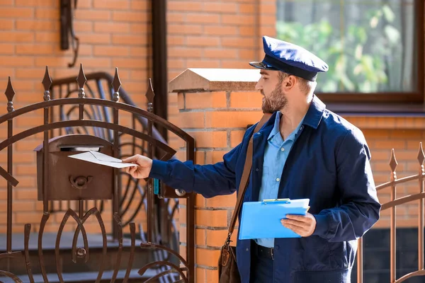 英俊的年轻邮递员把信放在室外的邮筒里 — 图库照片