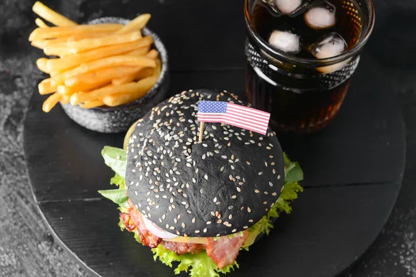 Tasty burger with black bun, french fries and cola drink on dark background