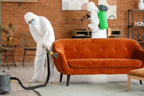 Workers in biohazard costume removing dirt from sofa in house