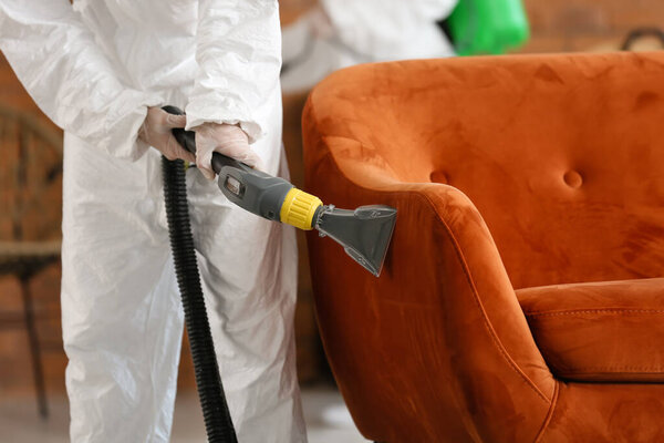 Worker in biohazard costume removing dirt from sofa in house