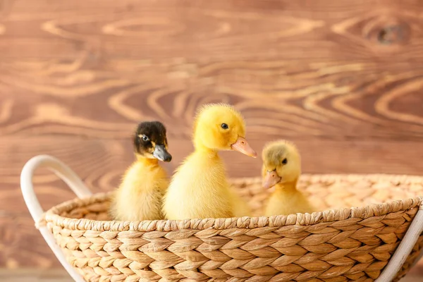 Cute ducklings in basket on wooden background