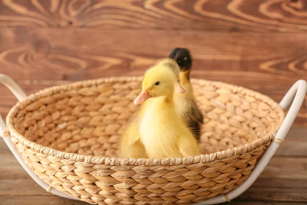 Cute ducklings in basket on wooden background