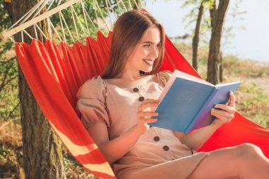 Dışarıda hamakta dinlenirken kitap okuyan genç bir kadın.