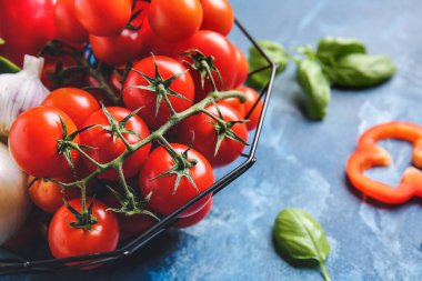 Taze kiraz domatesli sepet, bitki ve baharatlar renkli arka planda.