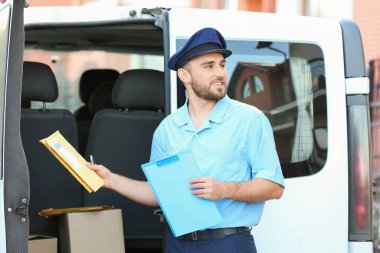 Arabasının yanında parselleri olan yakışıklı bir postacı.