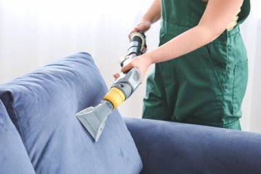 Kuru temizlemecinin çalışanı evdeki kanepedeki kiri temizliyor.