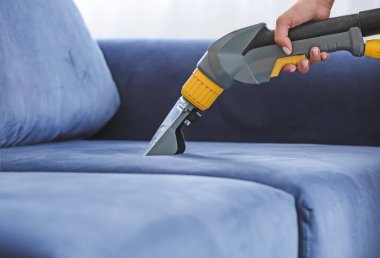 Kuru temizlemecinin çalışanı evdeki kanepedeki kiri temizliyor.