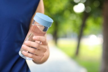 Parkta bir şişe suyu olan genç bir adam, yakın plan.